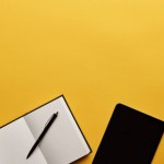 Top view of opened notebook and tablet on yellow surface