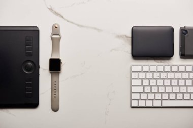 flat lay with graphics tablet with portable hdd, smart watch and wireless keyboard on white marble surface