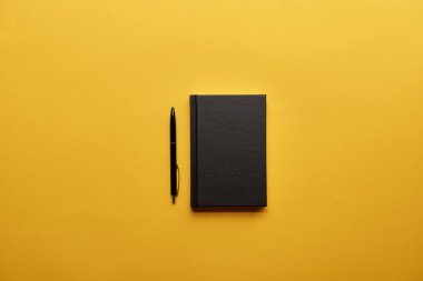 sarı yüzeyi kapalı defter ve kalem üstten görünüm