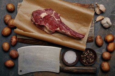 flat lay with raw rib eye steak on baking paper with butcher knife, spices, potatoes and garlic clipart