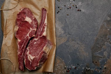 üstten görünüm çiğ Biftek Biftek pişirme kağıdı ile baharat gri arka plan üzerinde üzerinde