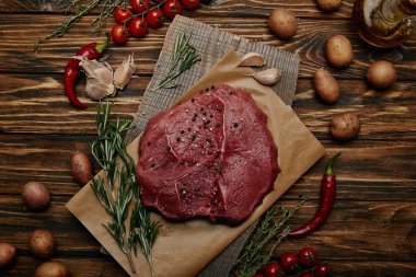 flat lay with raw meat on baking paper with vegetables and rosemary on wooden background clipart