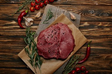 flat lay with fresh raw meat on baking paper with garlic and vegetables on wooden background clipart