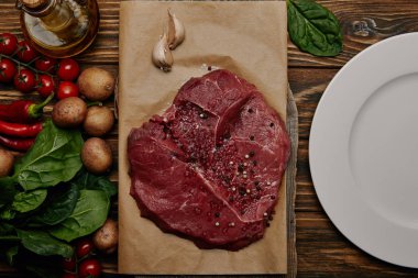 flat lay with fresh raw meat on baking paper with vegetables and spinach on wooden background clipart