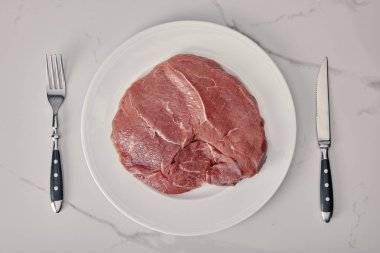top view of fresh raw meat on plate with kitchen cutlery on white background clipart