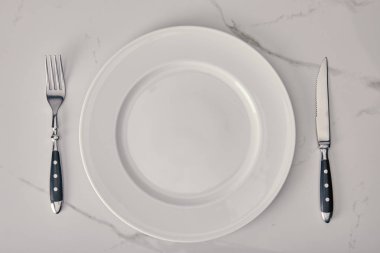 empty plate with fork and knife on white marble background clipart