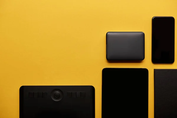 top view of graphics tablet with digital tablet, smartphone and portable hdd on yellow surface