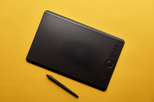 top view of graphics tablet and pen on yellow surface