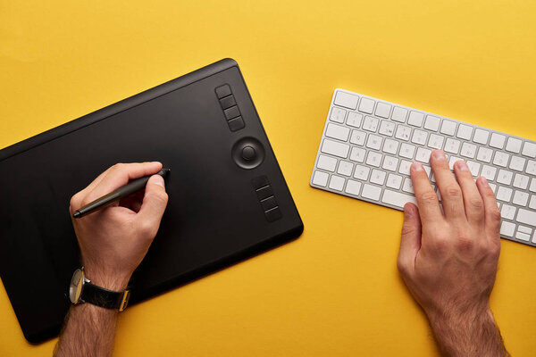 cropped shot of designer drawing with graphics tablet and keyboard on yellow surface