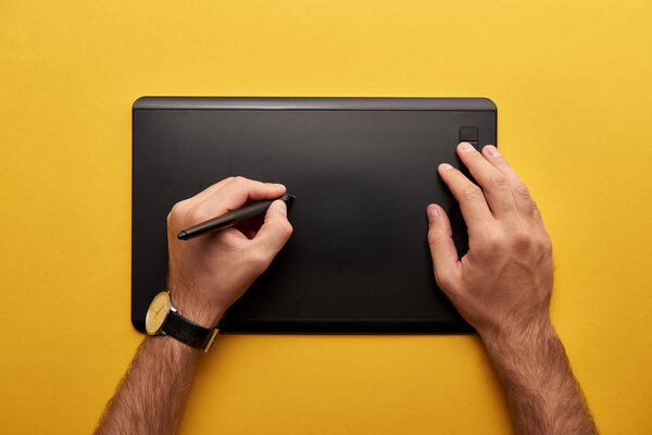 cropped shot of designer drawing with graphics tablet on yellow surface