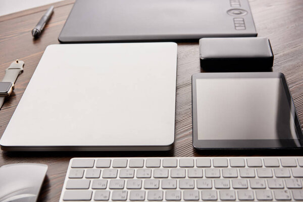 close-up shot of different wireless devices and graphics tablet on wooden desk