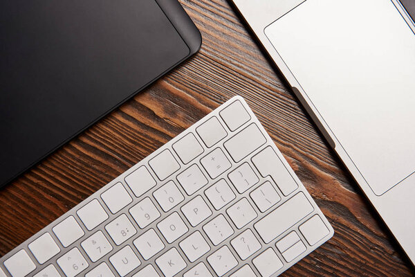 top view of laptop with wireless keyboard and graphics tablet on wooden table