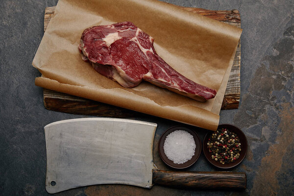 top view of raw rib eye steak on baking paper with butcher knife, spices 