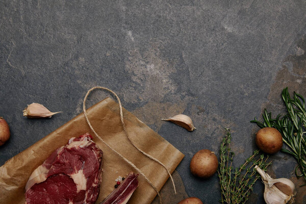 top view of raw meat steak on baking paper with potatoes on grey background