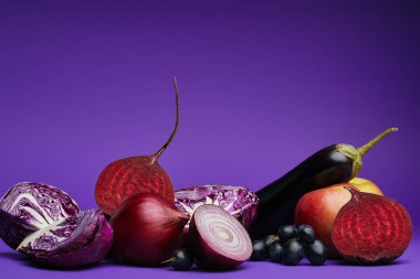 close-up view of sliced cabbage, onions, beetroot, grapes, apple and eggplant on purple  clipart