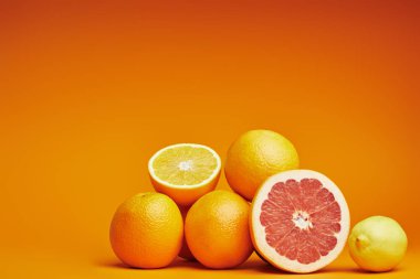 close-up view of fresh ripe whole and sliced citrus fruits on orange background clipart