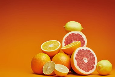 close-up view of fresh ripe whole and sliced citrus fruits on orange background clipart