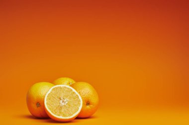 close-up view of fresh ripe whole and sliced oranges on orange background  clipart
