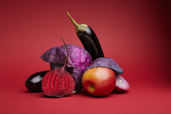close-up view of ripe organic apple, cabbage, eggplants, onion and beetroot on red background