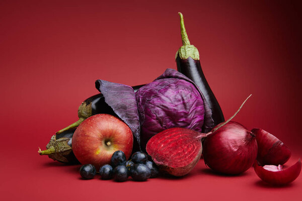 close-up view of ripe organic apple, grapes, onions, beetroot, cabbage and eggplants on red 