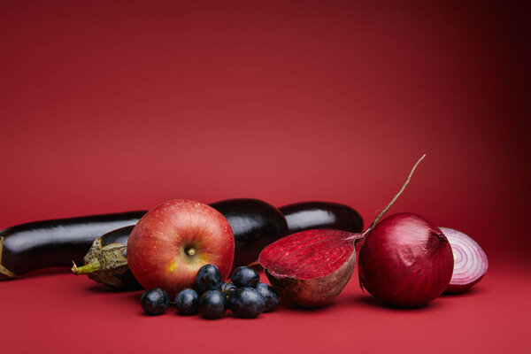 close-up view of fresh apple, grapes, eggplants, beetroot and onions on red background