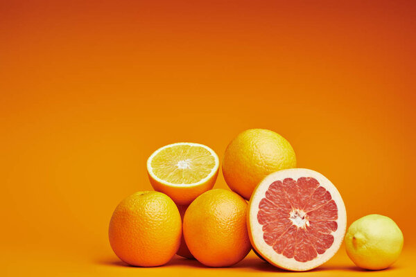 close-up view of fresh ripe whole and sliced citrus fruits on orange background
