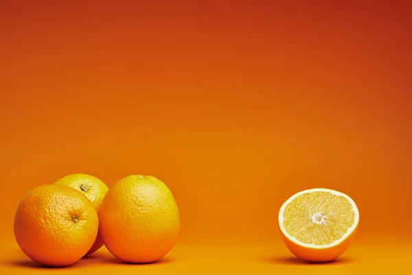 Nahaufnahme Ganzer Und Halbierter Orangen Auf Orangefarbenem Hintergrund — Stockfoto