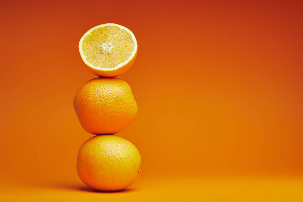 Крупный план цельных и нарезанных апельсинов на оранжевом фоне
 