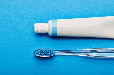top view of toothbrush and toothpaste arranged on blue backdrop, dentistry concept clipart