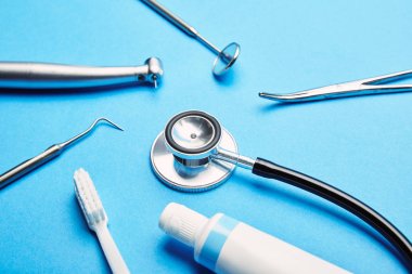 Steril diş aletleri, stetoskop, diş fırçası ve diş macunu diş bakımı kavramı mavi zemin üzerinde düzenleme görünümünü kapat