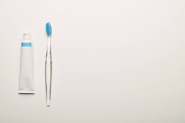 top view of toothbrush and toothpaste arranged on white backdrop, dentistry concept