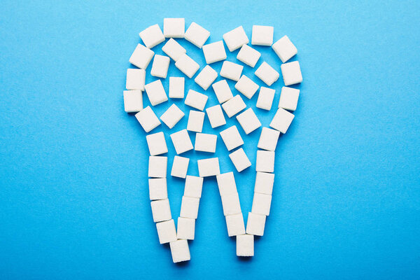 top view of white sugar cubes arranged in tooth sign on blue background, dental care concept