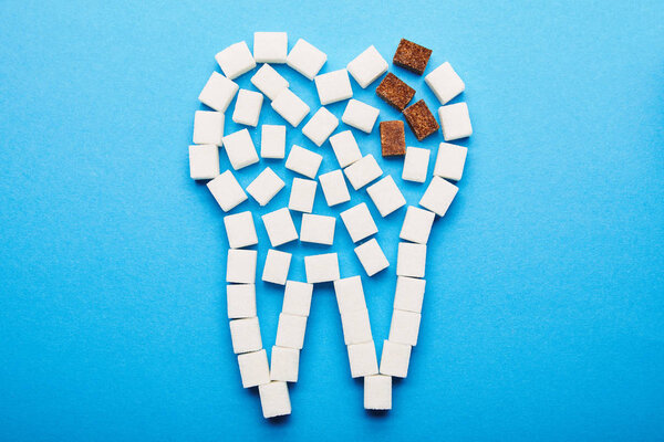 top view of white and brown sugar cubes arranged in tooth sign on blue background, dental caries concept