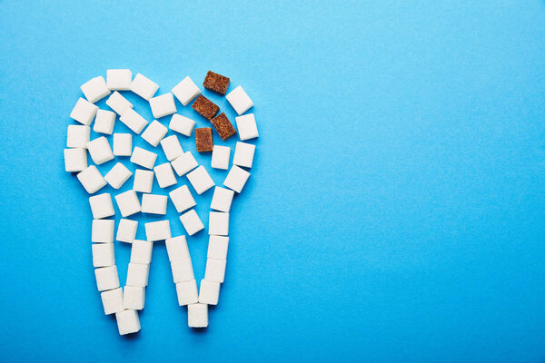 top view of white and brown sugar cubes arranged in tooth sign on blue background, dental caries concept