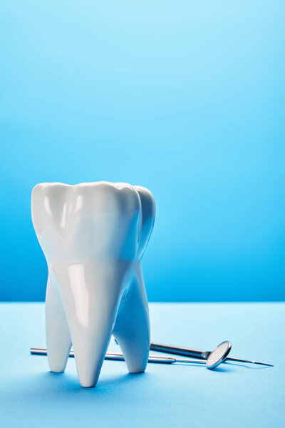 close up view of sterile dental mirror, probe and tooth model arranged on blue backdrop