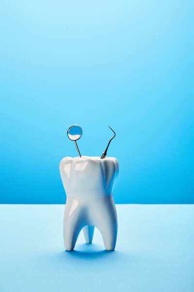 close up view of tooth model, dental mirror and probe on blue backdrop