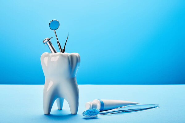 close up view of white tooth model, toothbrush, toothpaste and stainless dental instruments on blue backdrop
