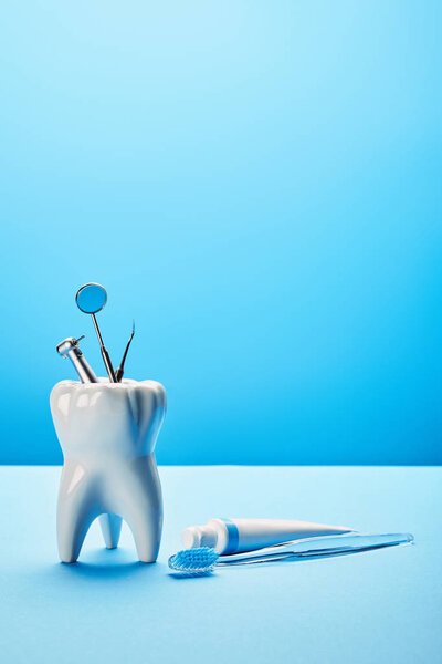 вид на белый зуб модели, зубной щетки, зубной пасты и нержавеющих зубных инструментов на синем фоне
