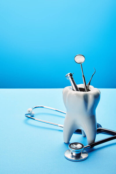 close up view of white tooth model, stethoscope and stainless dental instruments on blue backdrop