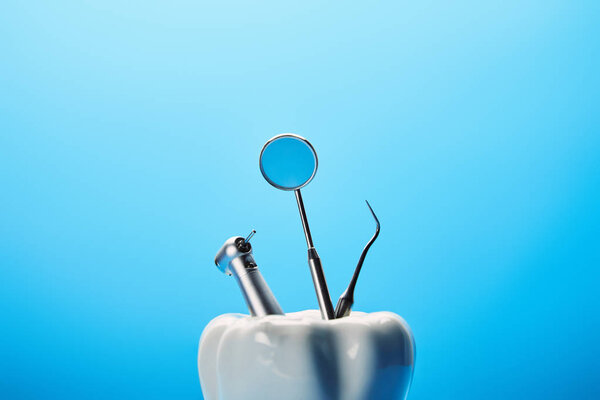 close up view of white tooth model and stainless dental instruments on blue backdrop