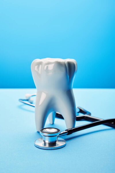 close up view of white tooth model and stethoscope on blue backdrop