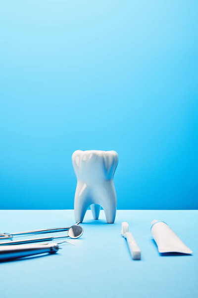 вид на белый зуб модели, зубной щетки, зубной пасты и нержавеющих зубных инструментов на синем фоне
