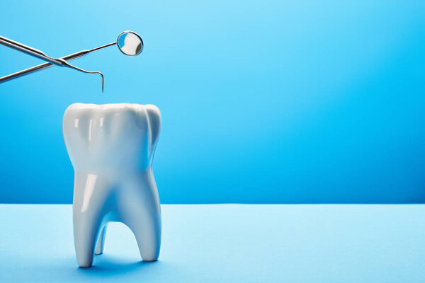 close up view of tooth model, dental mirror and probe on blue backdrop