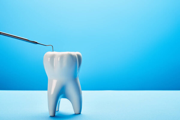 close up view of tooth model and dental probe on blue background