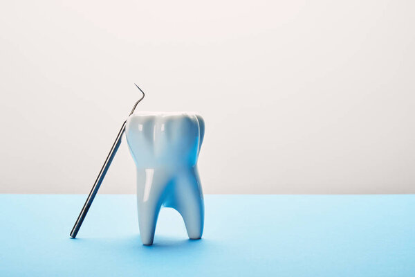 близкий обзор модели зуба и зубного зонда на синем и белом фоне
