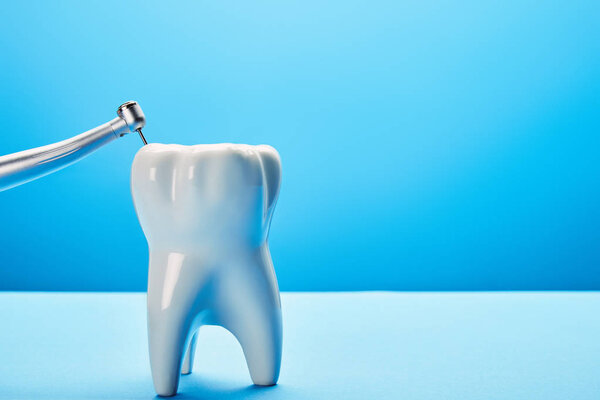 close up view of dental drill and white tooth model on blue background, dentistry concept