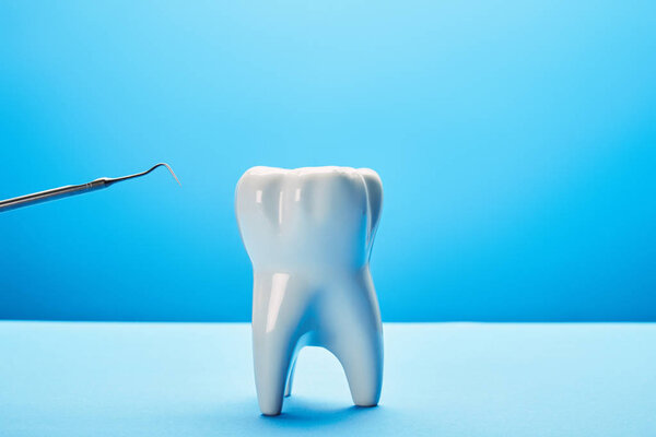 close up view of tooth model and dental probe on blue background