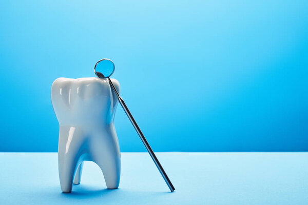 close up view of tooth model and dental mouth mirror on blue backdrop