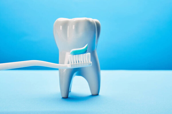 close up view of tooth model and toothbrush with paste on blue background, dental care concept