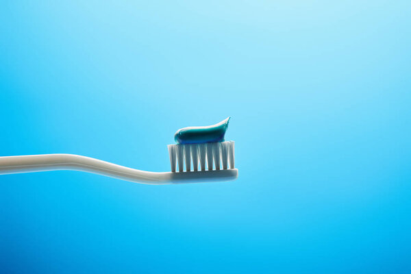 close up view of toothbrush with paste on blue backdrop